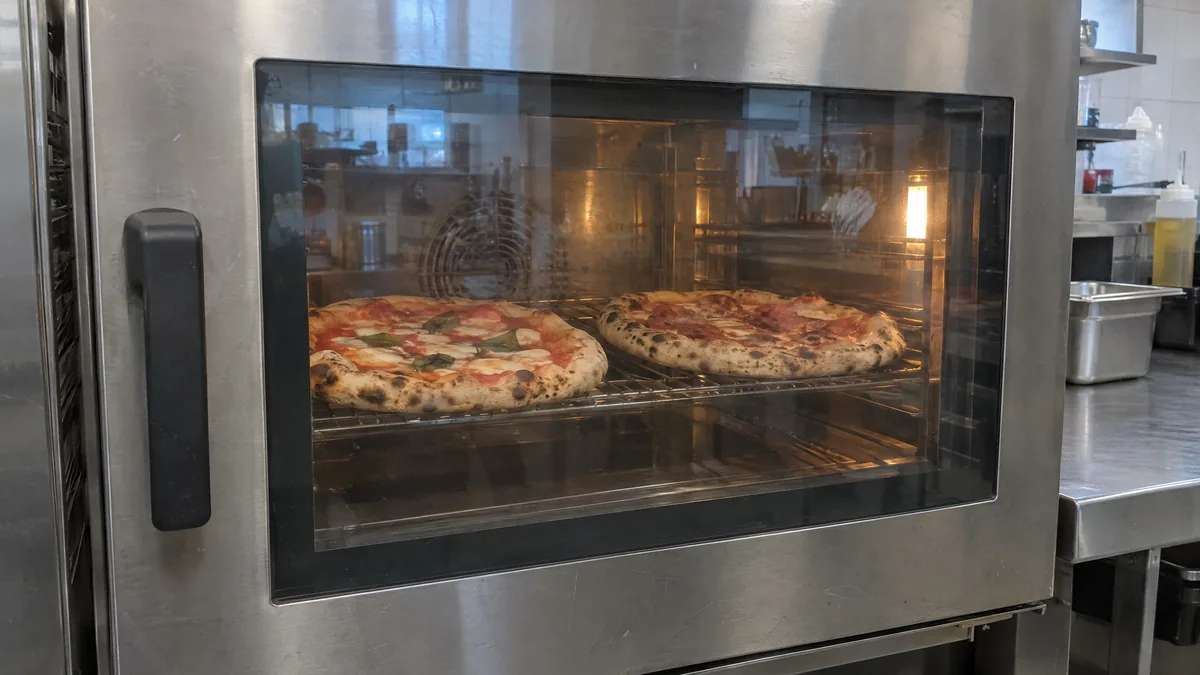 Kombidämpfer in einer Profiküche: Durch die Glastür sieht man eine Pizza Margherita und eine Pizza Salami auf dem Rost